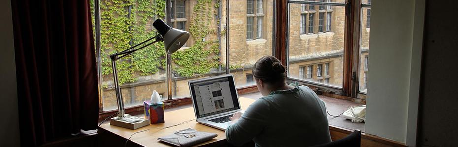 一名学生坐在窗户边的桌子上学习，可以俯瞰三一学院的校园
